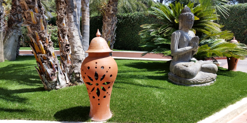 Réalisation en gazon synthétique dans un jardin avec statue et palmier
