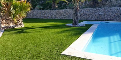 Pelouse artificielle autour d'une piscine avec palmier et mur en pierre